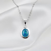 A silver oval pendant necklace featuring a vibrant blue iridescent opal stone, displayed on a draped white satin fabric background.