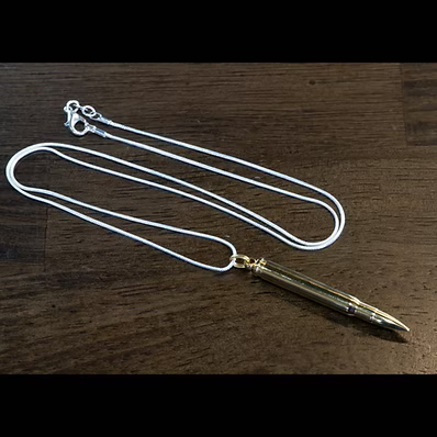 A silver snake chain necklace with a gold-toned bullet pendant, displayed on a dark wood background.