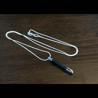 A silver chain necklace with a black cylindrical pendant, photographed on a dark brown wooden surface.