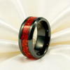 A black ceramic ring with a textured red inlay, displayed on a draped white satin fabric background.