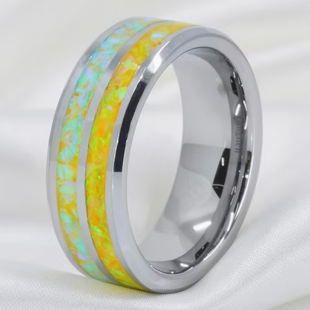 A polished silver-toned band ring featuring a vibrant yellow and green iridescent inlay with a thin white stripe, resting on a soft white fabric background.