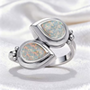 A silver ring featuring two overlapping teardrop-shaped opal stones with iridescent multicolor play-of-color, set in polished silver bezel settings on a white satin background.