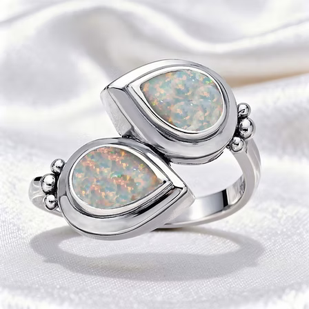 A silver ring featuring two overlapping teardrop-shaped opal stones with iridescent multicolor play-of-color, set in polished silver bezel settings on a white satin background.