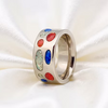 A silver band ring decorated with multiple oval and round colorful gemstones in red, blue, green, and orange, displayed on a white satin fabric background.