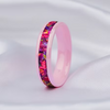 A pink band ring with a colorful floral inlay, resting on a soft white satin fabric background.