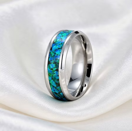 A polished silver-toned band ring with a vibrant blue and green iridescent inlay, displayed on a draped white satin fabric.