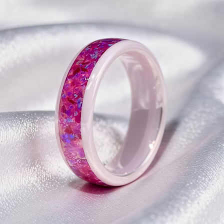 A pink band ring with a vibrant magenta and purple iridescent opal inlay, resting on a soft, white textured fabric background.