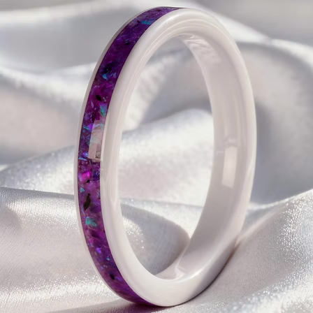 A white ceramic ring with a vibrant purple and iridescent blue inlay, displayed on a draped white satin fabric.