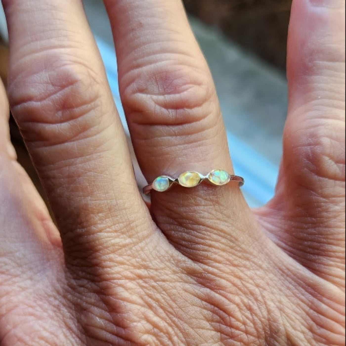 A close-up of a person's hand wearing a delicate silver ring with three small, round, iridescent white beads on the ring finger.