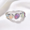 A silver ring featuring five oval opal gemstones in a row, each displaying vibrant iridescent colors like pink, purple, blue, and green, set against a soft white fabric background.