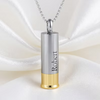A silver cylindrical pendant necklace with a gold bottom, engraved with the name 'Robert', hanging from a silver chain against a draped white satin background.