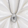 A silver teardrop-shaped pendant necklace with a black engraved letter 'E' on a silver chain, displayed on a white satin fabric background.