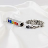 A silver metal cremation urn pendant with six colorful enamel inlays (blue, green, yellow, orange, red) and a matching silver chain, displayed on a draped white fabric background.