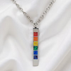 A silver-toned chakra necklace with a vertical rectangular pendant featuring seven colorful inlay squares in red, orange, yellow, green, blue, and purple, displayed on a white satin fabric background.