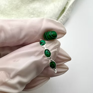 A silver ring with three green malachite gemstone accents, held between a hand