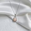 A silver teardrop pendant necklace with a milky white iridescent opal inlay, displayed on draped white satin fabric.