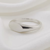 A polished silver signet ring with a smooth, rounded oval face and a tapered band, resting on a soft, draped white fabric background.