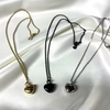 Three heart-shaped pendant necklaces displayed on draped white satin fabric, shown in gold, black, and silver tones.