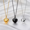 Three heart-shaped pendant necklaces displayed on draped satin fabric, featuring gold, black, and silver finishes.