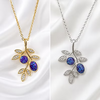 Two leaf-shaped pendant necklaces displayed side by side on a white satin background. The left necklace is gold-toned with two oval blue opal stones and small clear crystal accents.