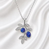A silver-toned branch-shaped pendant necklace featuring two oval deep blue opal gemstones and small clear crystal leaves, displayed on a white satin fabric background.