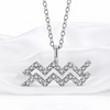 A silver-toned necklace with a pendant shaped like the Aquarius zodiac sign, adorned with small clear stones, displayed on a soft white satin fabric background.