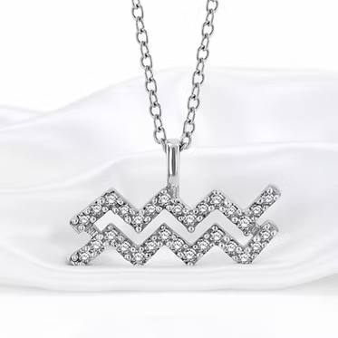 A silver-toned necklace with a pendant shaped like the Aquarius zodiac sign, adorned with small clear stones, displayed on a soft white satin fabric background.
