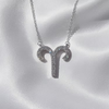 A silver-toned Aries zodiac sign pendant necklace adorned with small clear crystals, displayed on a soft white satin fabric background.