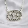 A silver-tone necklace with a Gemini zodiac symbol pendant, embellished with clear rhinestones, displayed on a white satin fabric background.