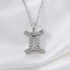 A silver-tone Gemini zodiac sign pendant necklace adorned with small clear crystals, resting on a white satin fabric background.