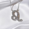 A silver-tone necklace with a Leo zodiac symbol pendant, set with sparkling clear crystals, is displayed on draped white satin.