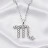 A silver-toned Zodiac sign pendant necklace featuring the Scorpio symbol, embellished with small clear stones, displayed on a white satin fabric background.