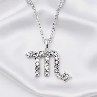 A silver-toned Zodiac sign pendant necklace featuring the Scorpio symbol, embellished with small clear stones, displayed on a white satin fabric background.