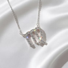 A silver-toned necklace with a Virgo zodiac sign pendant, embellished with sparkling clear crystals, is displayed on a draped white satin fabric.