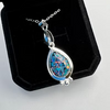 A teardrop-shaped pendant necklace featuring a vibrant blue, green, and orange iridescent opal stone in a polished silver bezel, displayed on a black velvet jewelry box.