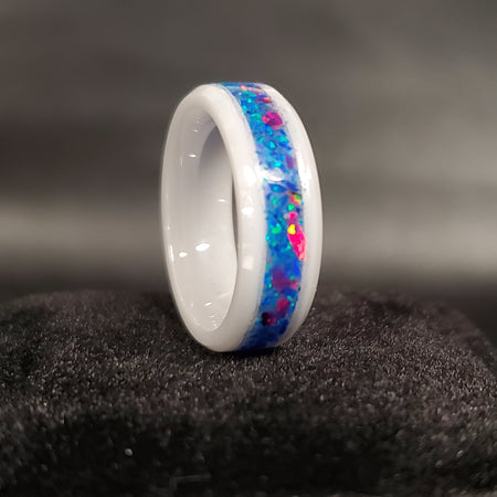 A white ceramic glow ring with blue and multicolored ash inlays, set on a black textured background.